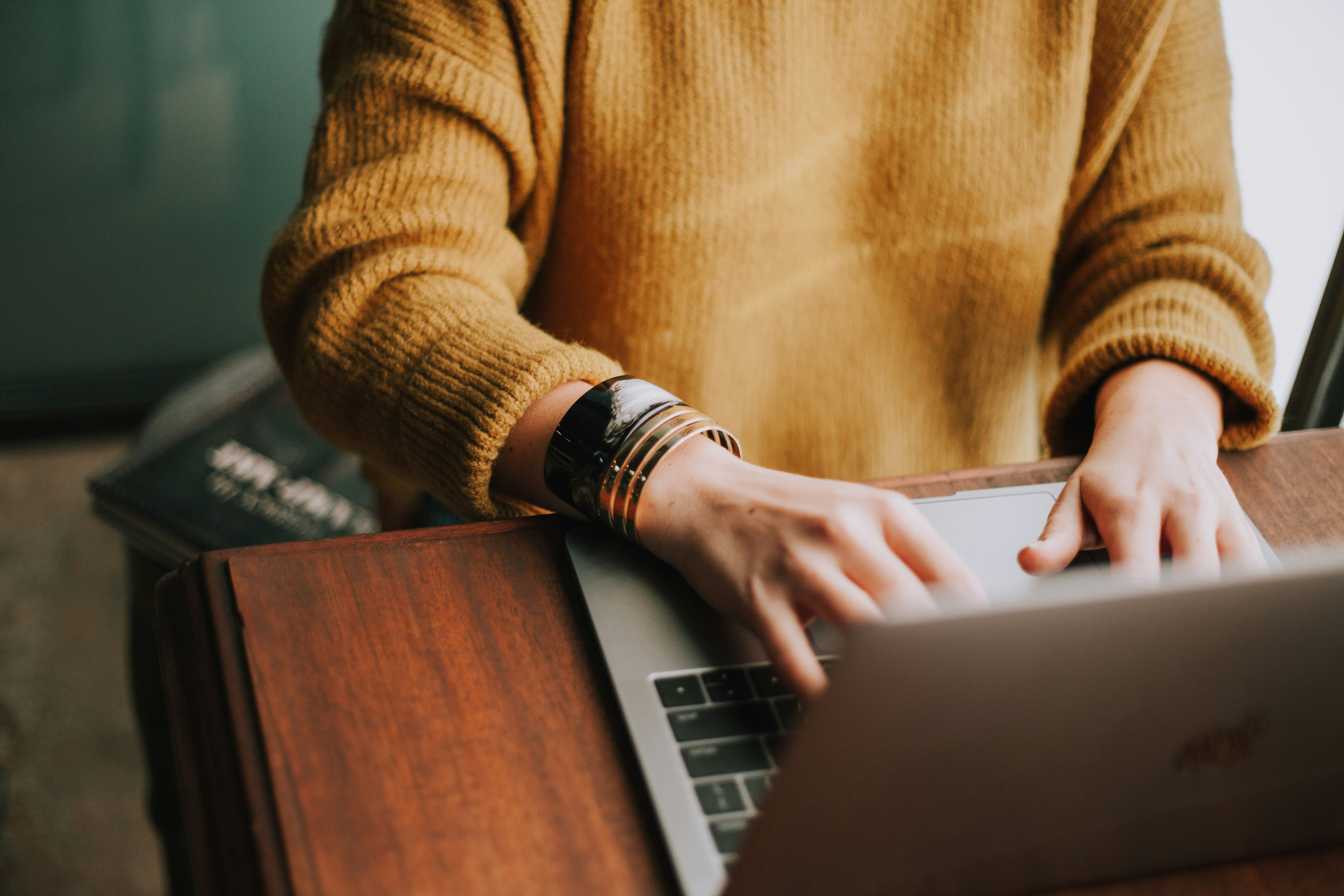 woman typing on computer in yellow sweater